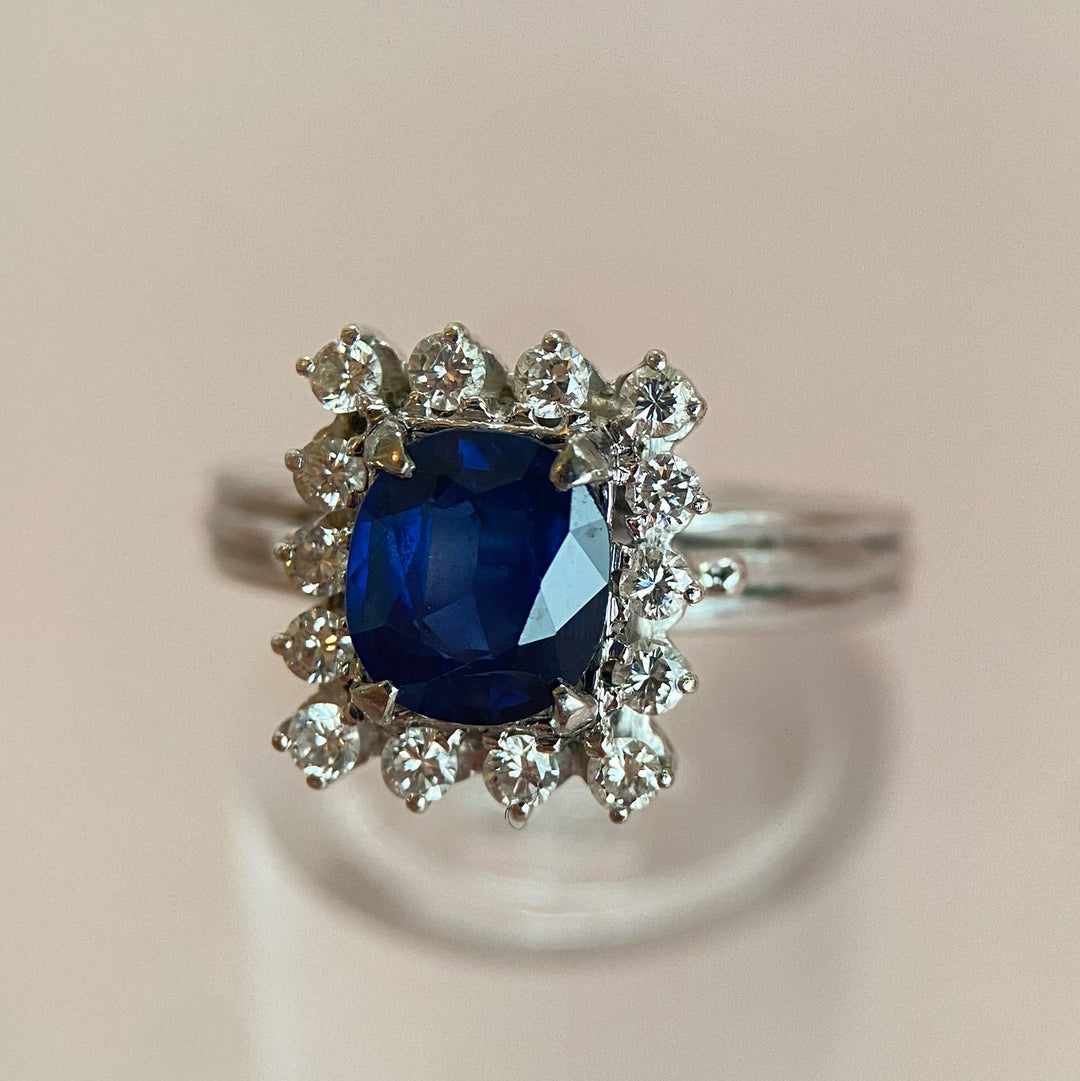 Detailaufnahme des tiefblauen, facettierten Kissenschliff‑Saphirs im Weißgoldring mit Diamanten in Krappenfassungen, intensive Farbe erkennbar