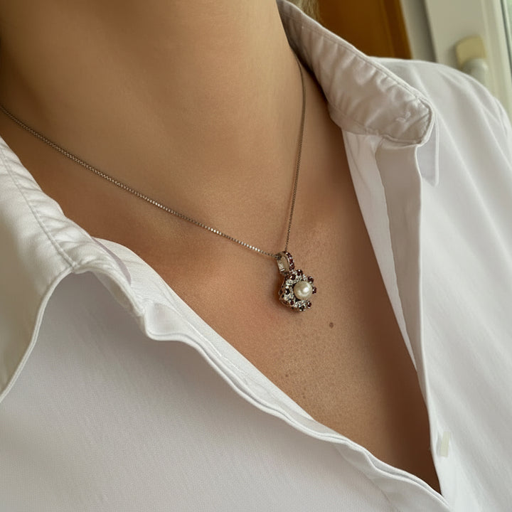 Tragefoto: Weißgoldener Clip‑Pendant mit Zuchtperle und Rubinen an Kette getragen, zeigt elegante Wirkung am Dekolleté