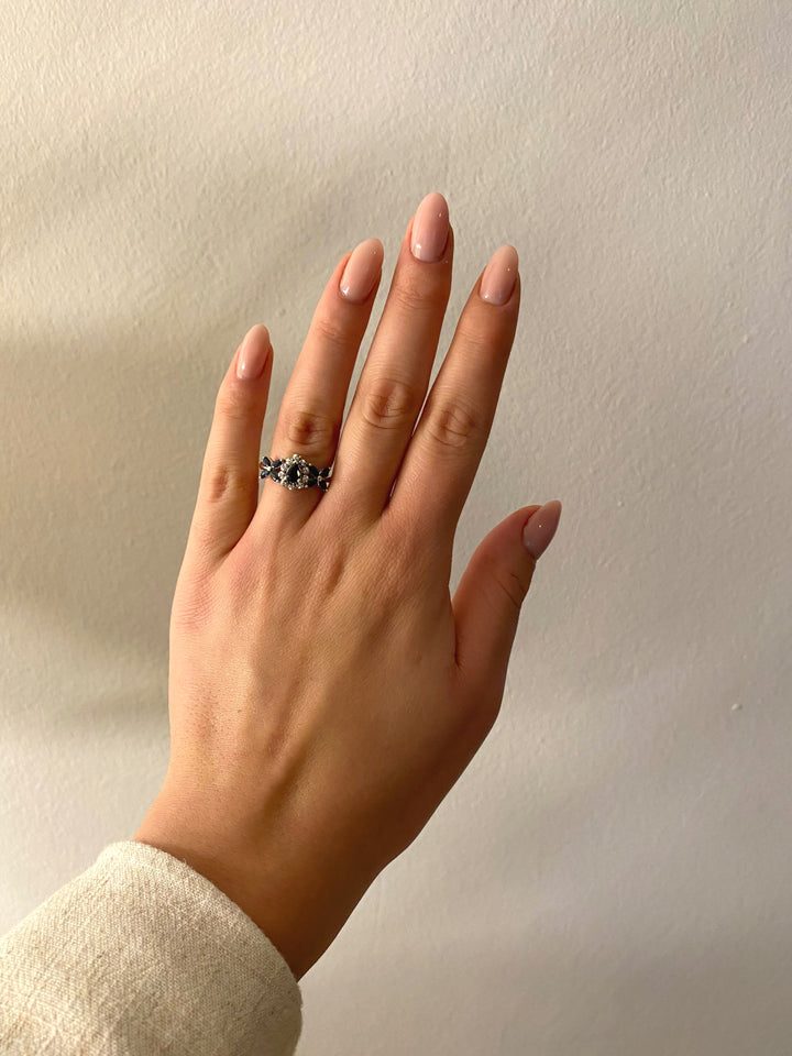 Tragefoto: Weißgoldring mit dunkelblauen Saphiren und Diamanten am Finger getragen, Wirkung und Stil erkennbar