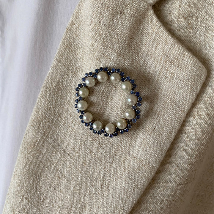 Detailansicht der Weißgold-Brosche mit Krappenfassungen, leuchtend blauen Saphiren und feinem Lüster der Akoya-Perlen.
