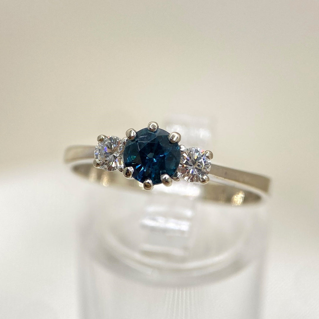 Seitenansicht links eines 585er Weißgoldrings mit grünlich-blauem Saphir und Diamanten in Krappenfassung