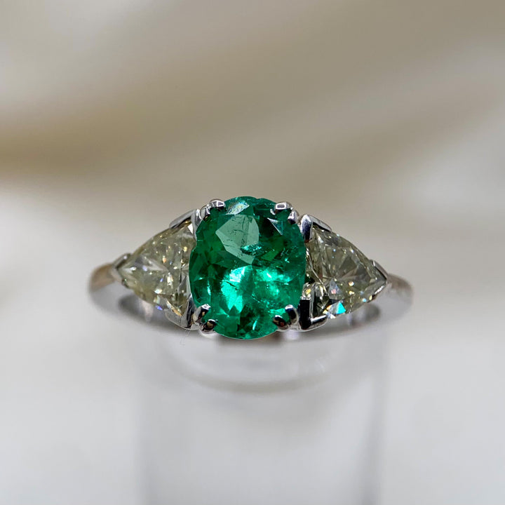 Nahaufnahme des Weißgoldrings mit 1,53 ct Smaragd im Ovalschliff und zwei Trilliant-Diamanten, die die Facetten, Krappenfassungen und Farbintensität des Edelsteins deutlich zeigt.